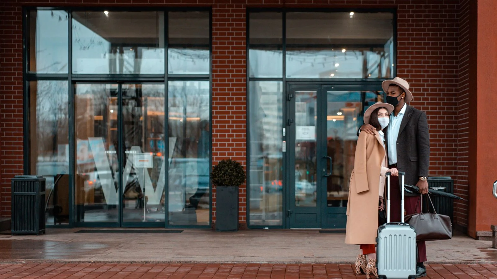 A couple arriving at a hotel entrance with luggage, the traveler behind every destination story an editor assigns.