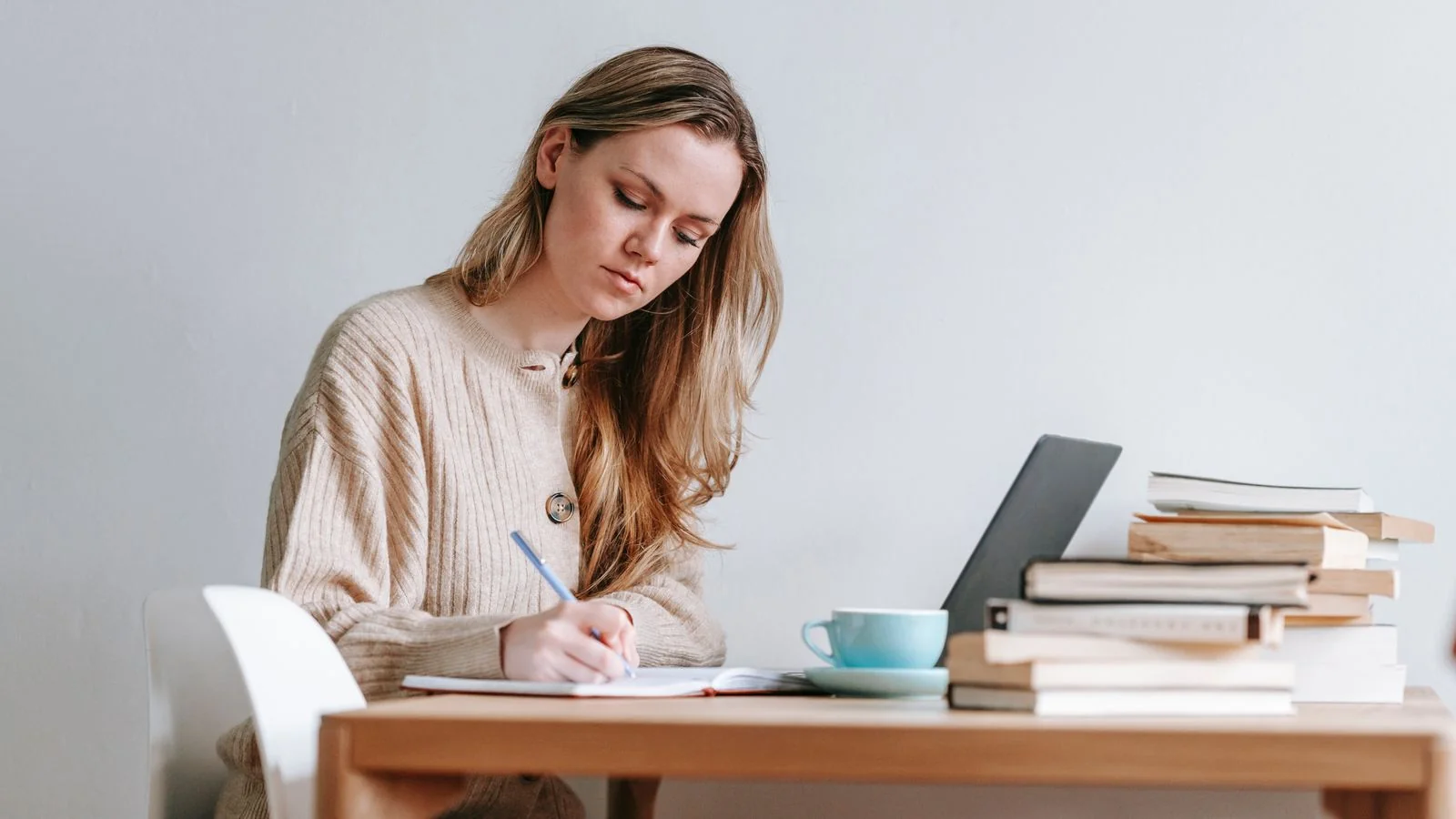 A focused writer taking handwritten notes beside an open laptop and stacked books