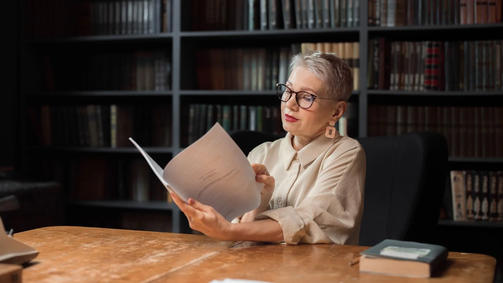 An editor reading a printed manuscript at a desk in a quiet, book-lined room