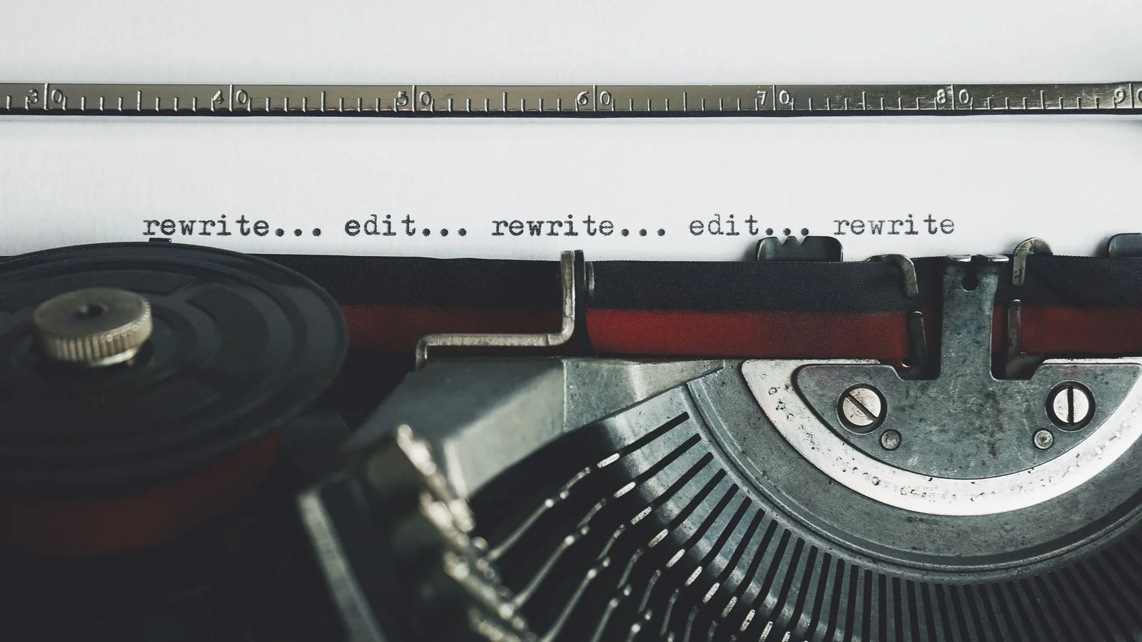A vintage typewriter with a sheet reading rewrite and edit, mid-revision on a wooden desk