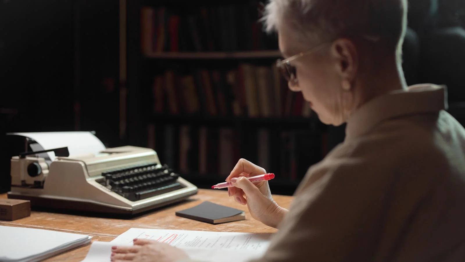 Editor reviewing a manuscript with red pen marks at a wooden desk