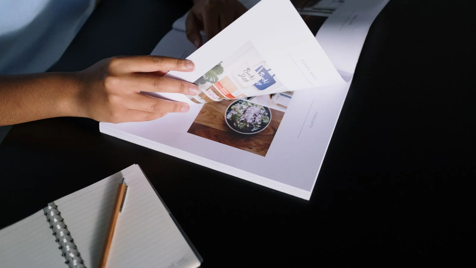 Hands flipping through a glossy magazine beside a notepad, the editorial review that happens before publication