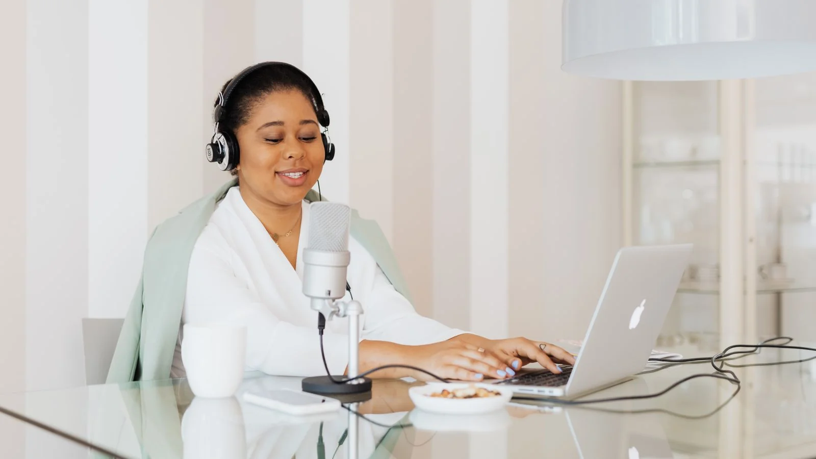 Smiling woman presenting on a laptop with a microphone at a bright home office desk