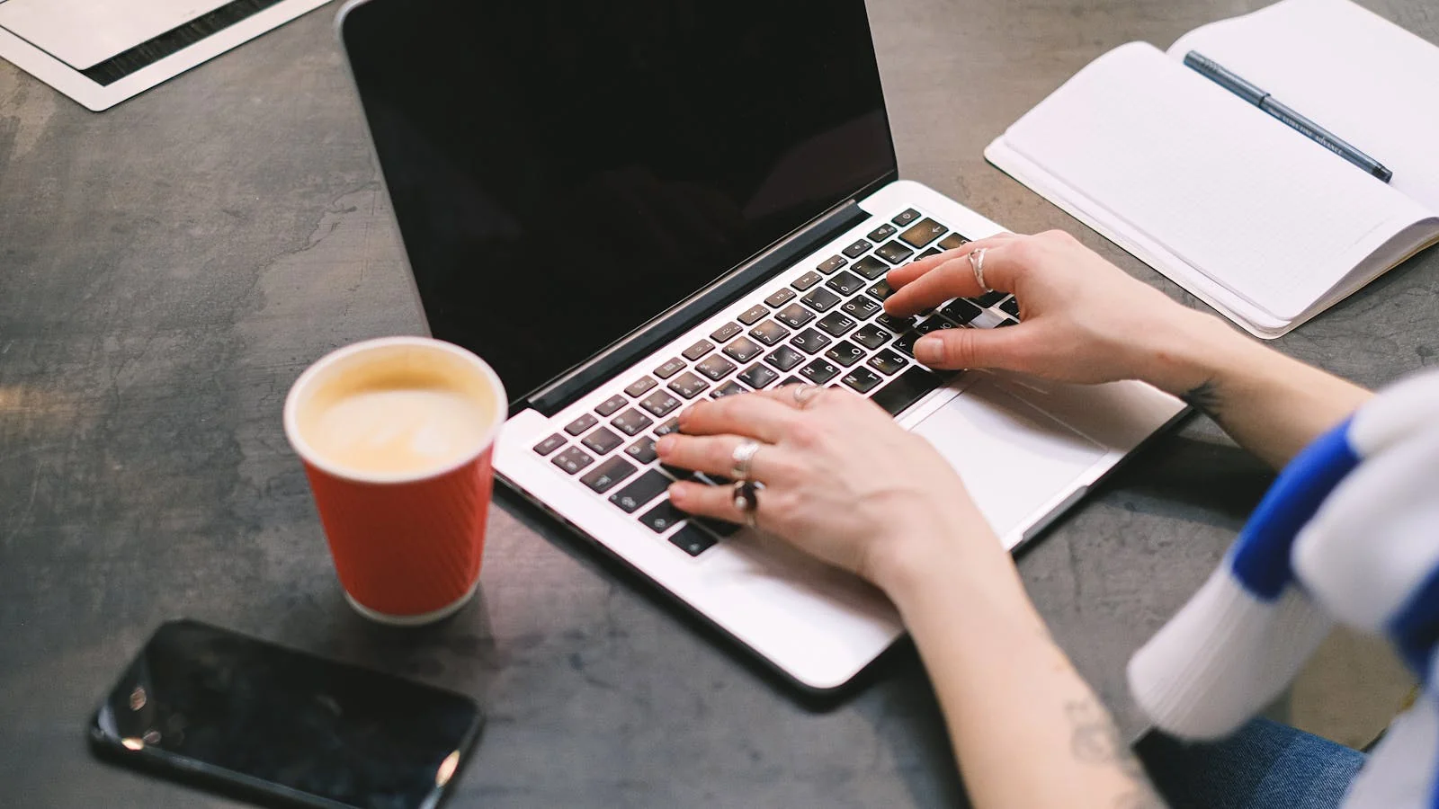 A freelancer typing at a laptop with coffee and a notepad, the depth every issue has to deliver.