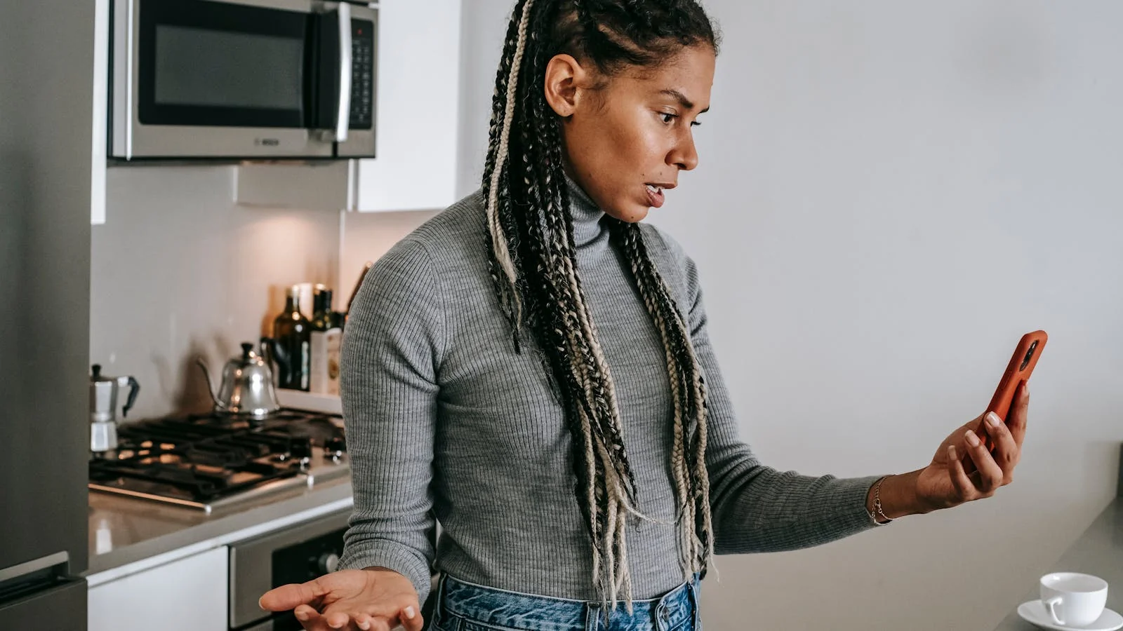 Frustrated customer reviewing a product on her smartphone with a critical expression while sitting in a kitchen