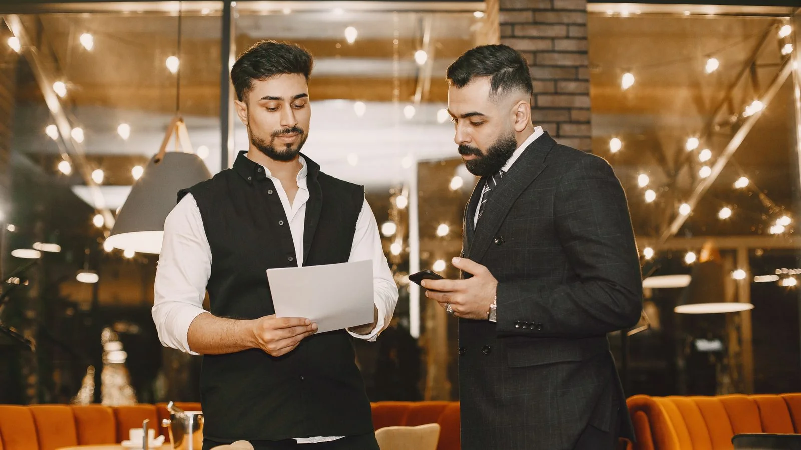 Two people reviewing documents and a phone at a restaurant table in warm light