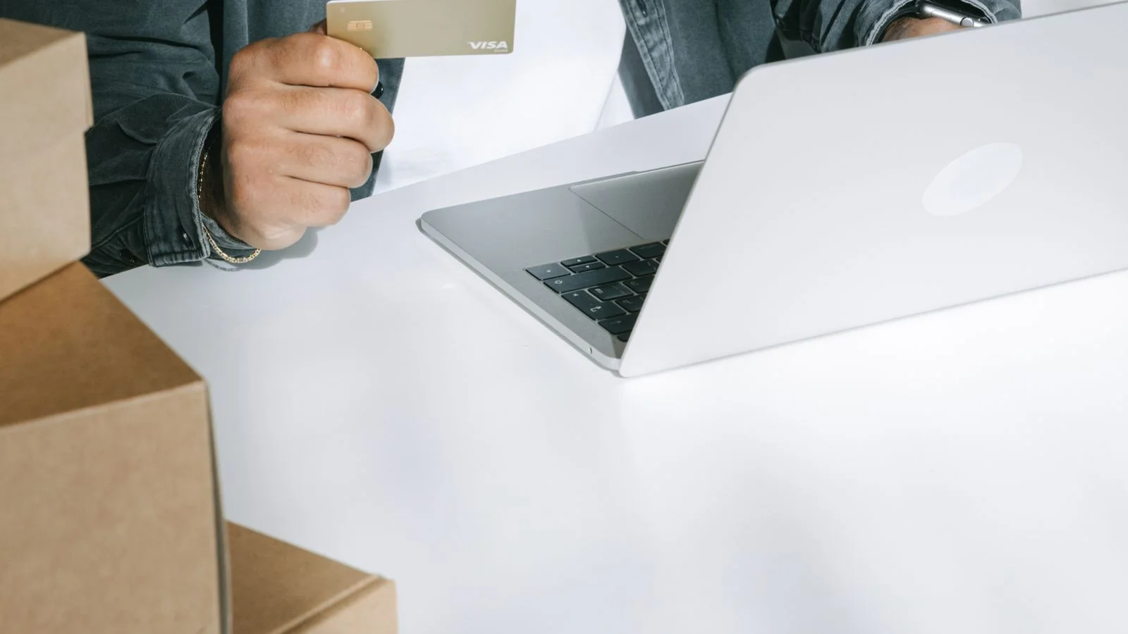 A person using a credit card to shop online on a laptop surrounded by boxes