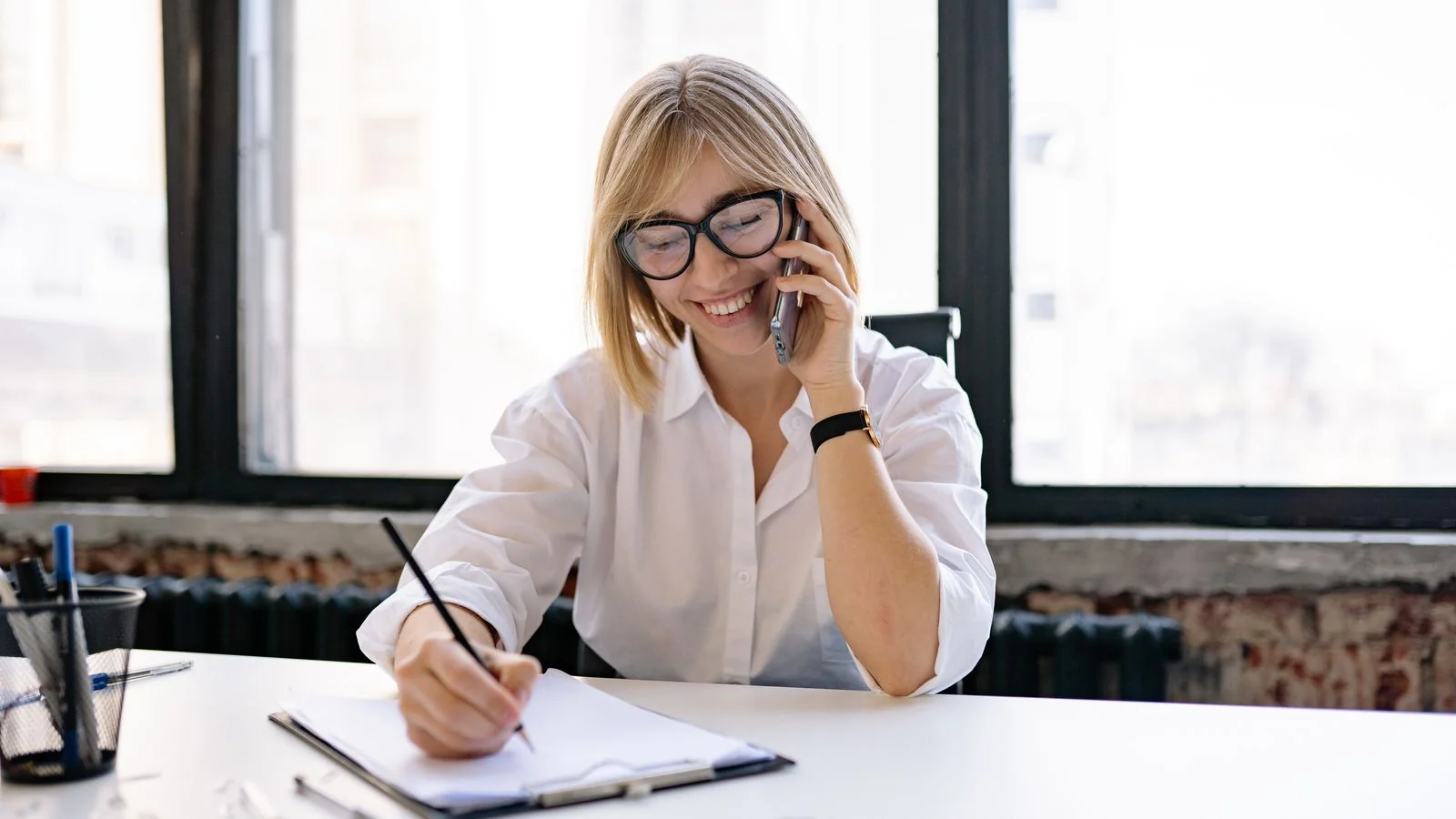A woman taking notes during a phone call at her desk, the reporter on the other end of a data pitch