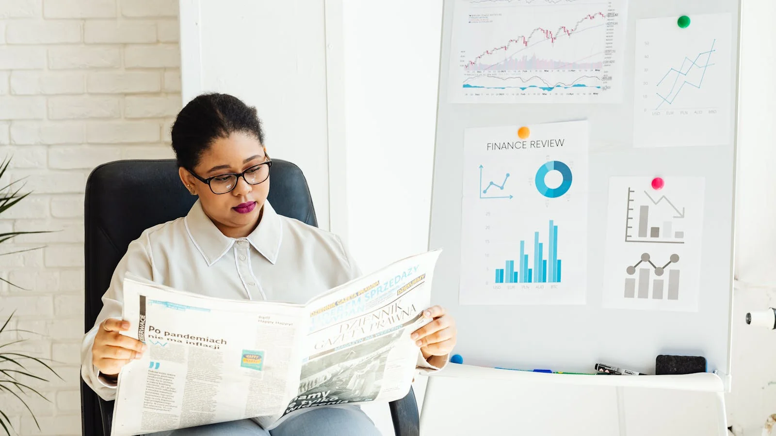 A reader studying a newspaper with stock charts, the recession story every newsroom is chasing
