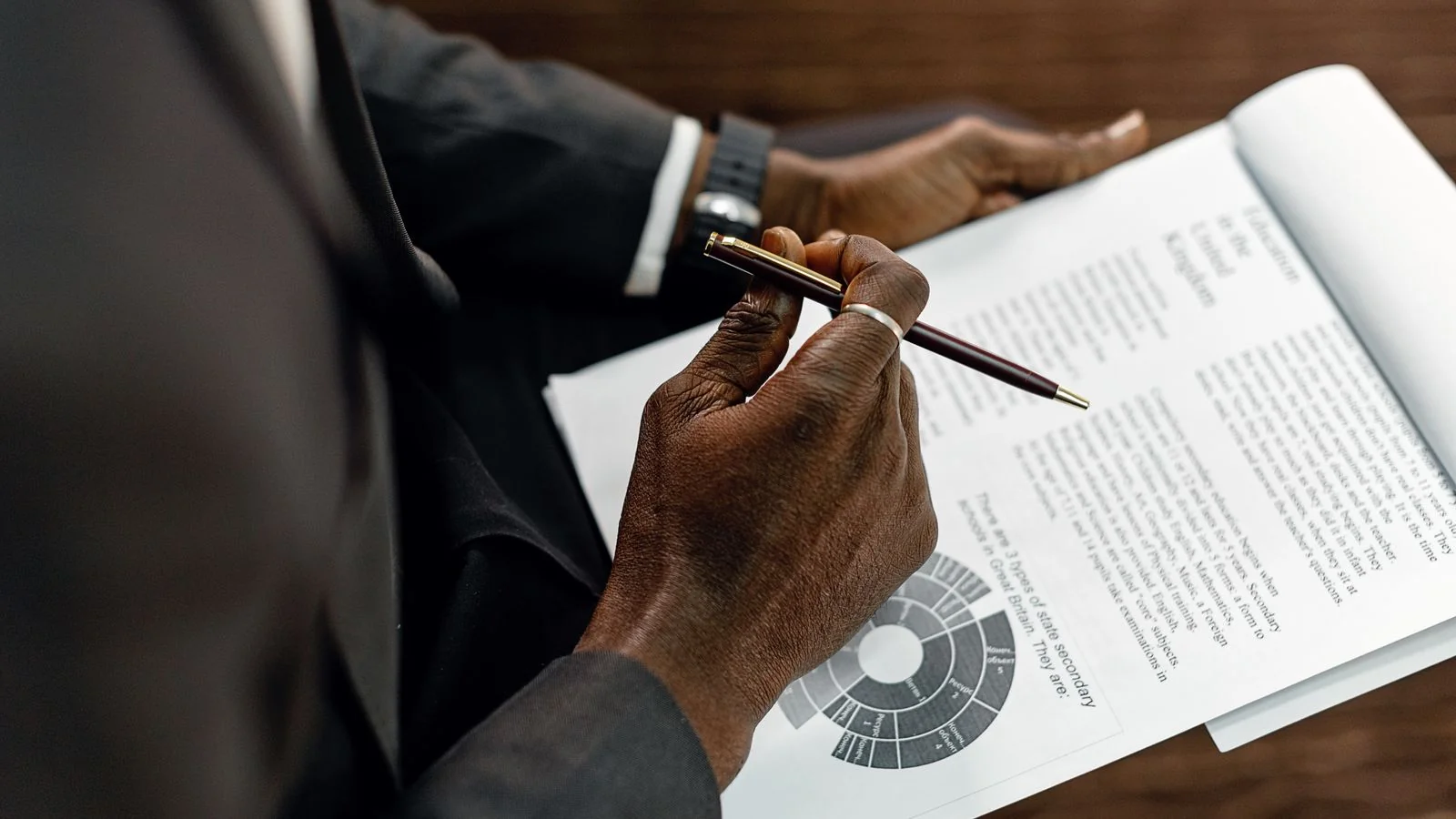 Person in a suit reviewing a printed manuscript with a pen, editing line by line