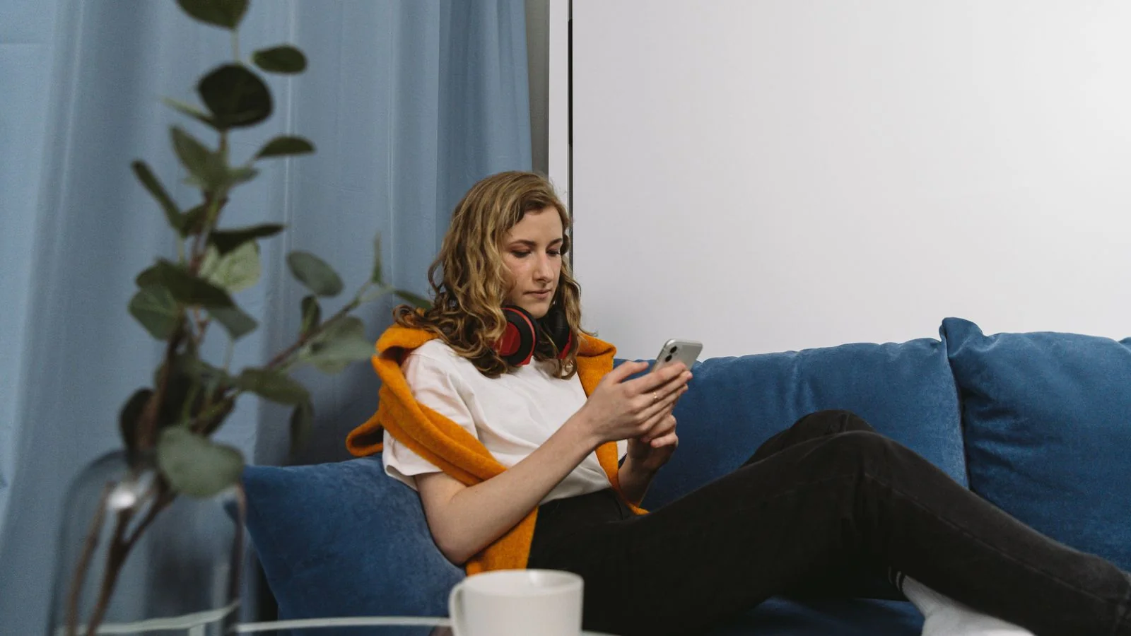 A woman on a blue couch scrolling her phone past most of what she sees.