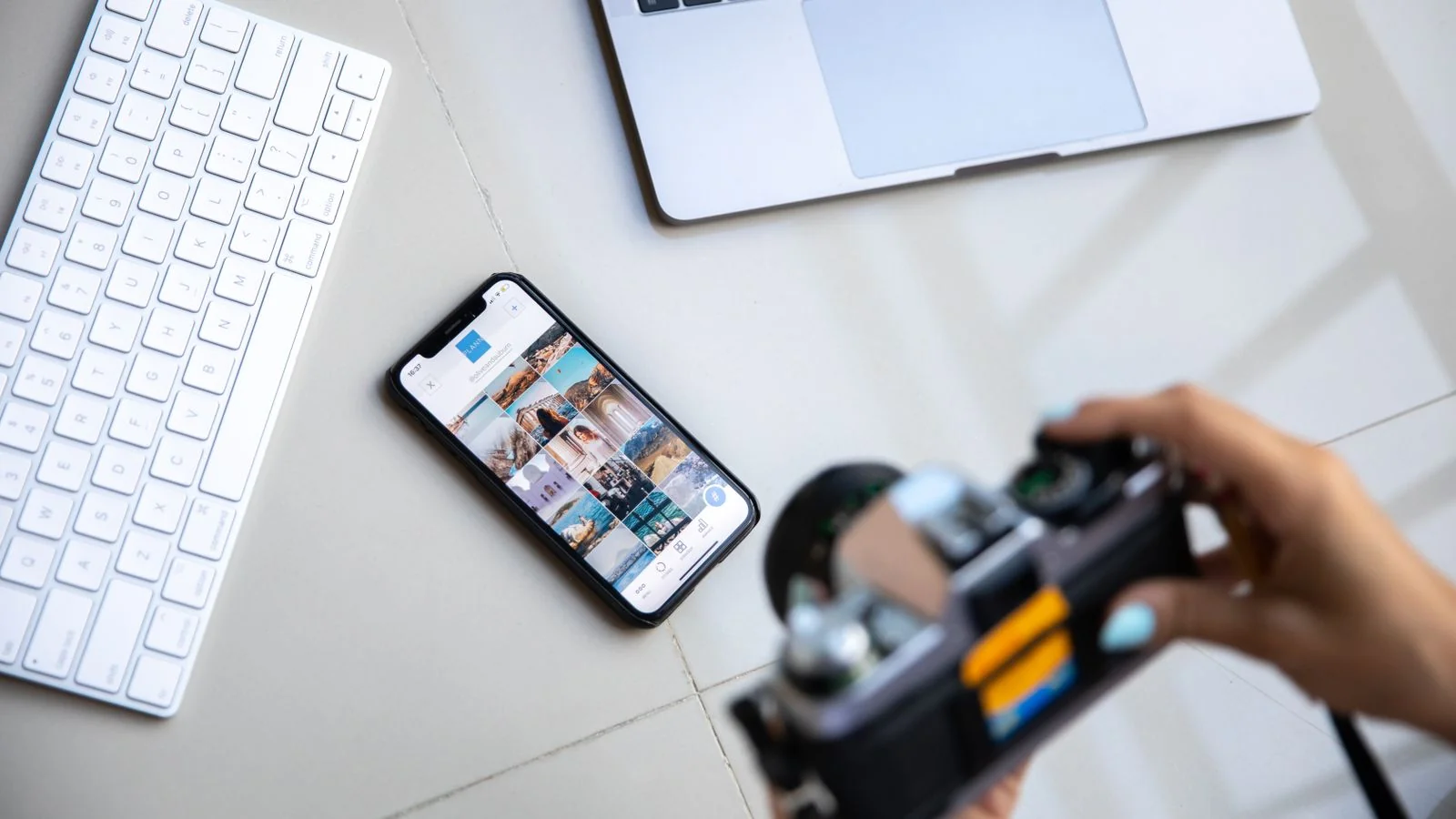 A person arranging a smartphone, laptop, and camera in a creative flat lay