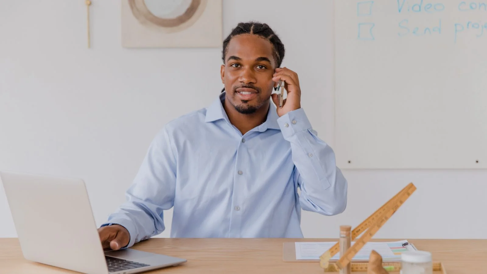Business owner smiling while using a laptop and phone, handling a customer issue without defensiveness
