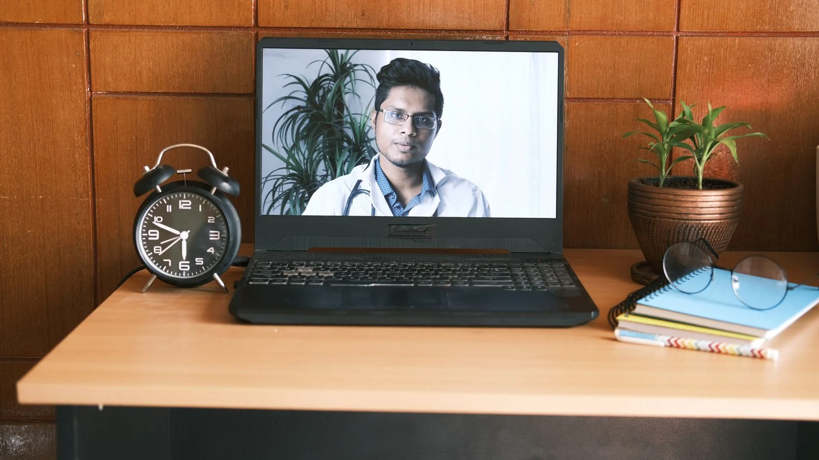 A home office desk with a laptop open on a video call, where most source interviews now happen