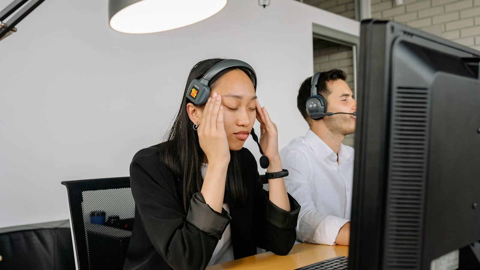 Stressed customer service agent at a call center desk with eyes closed in frustration