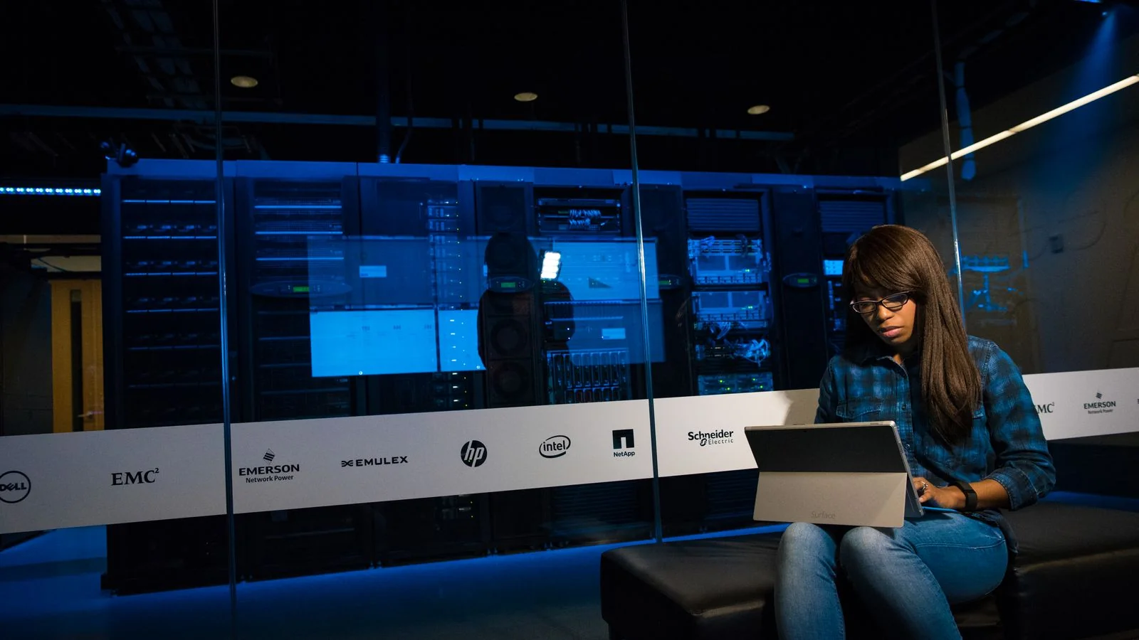 A woman working on a laptop inside a server room, representing infrastructure-scale content production