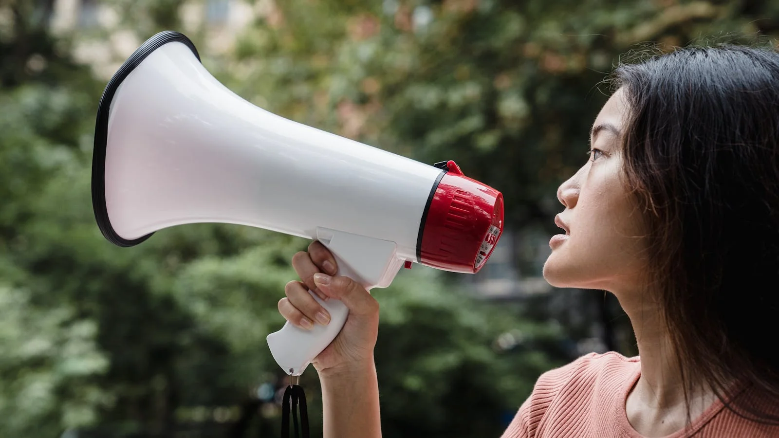 Side view of a woman holding up a megaphone outdoors, the kind of small first action a movement founder takes when announcing the alternative.
