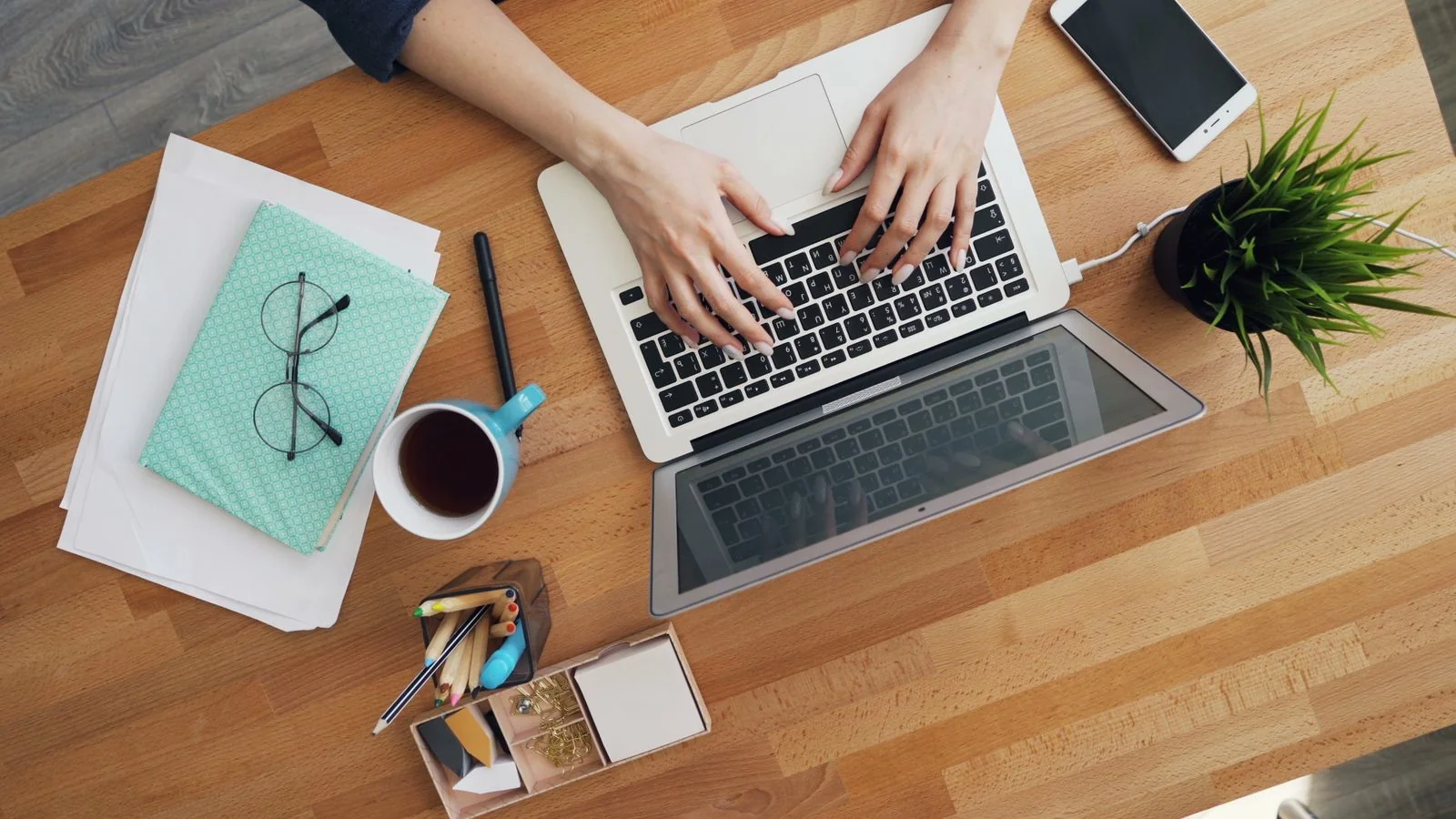 Overhead view of a modern desk with a laptop, coffee, and accessories mid-workflow