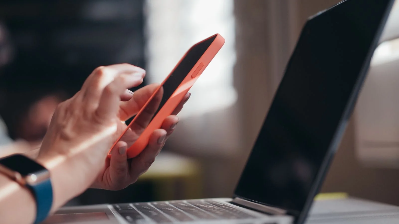 A person using a smartphone and laptop together on a desk
