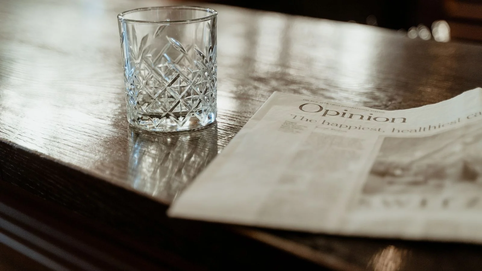 A newspaper resting on a polished bar counter next to a crystal glass, suggesting the reading environment a byline competes in