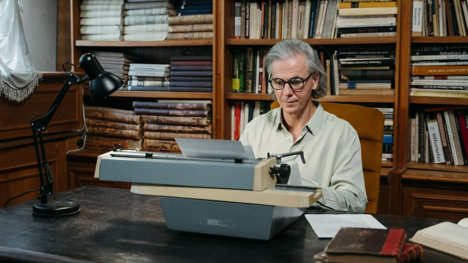 An elderly writer using a typewriter in a vintage library filled with bookshelves