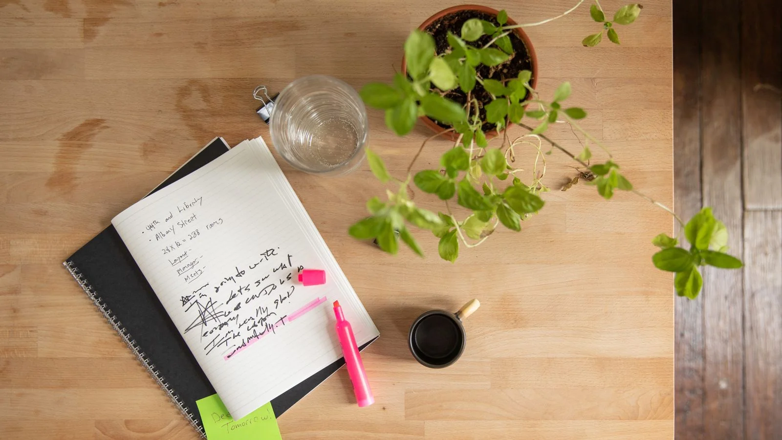 Overhead view of a tidy desk with an open notebook, a highlighter, and a small plant