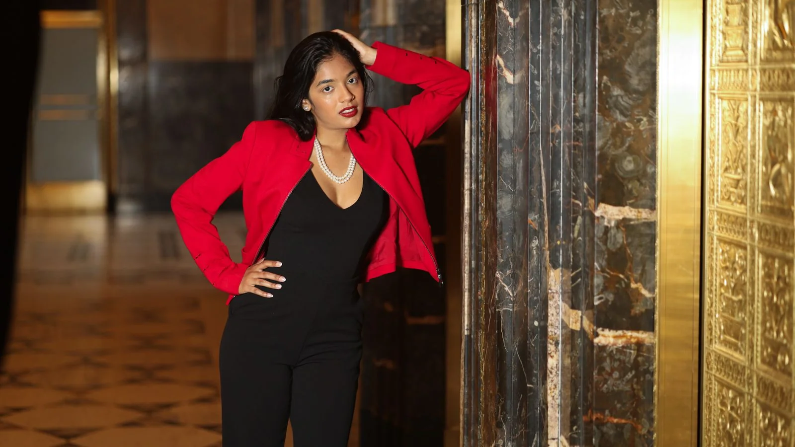 Woman in a red jacket standing with composure in an elegant interior, presenting a deliberate first impression
