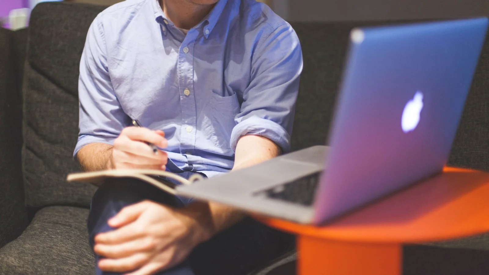 Person drafting notes with a laptop on a couch, planning the coverable moments of an event