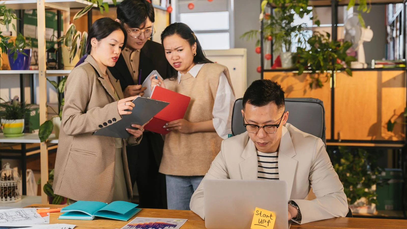 Two colleagues review launch notes together at a plant-filled desk