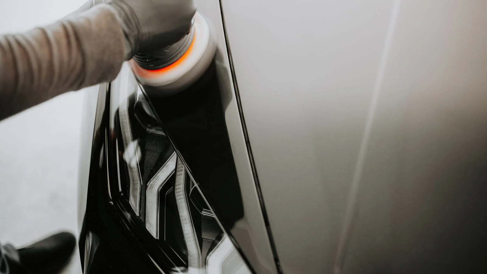 Close-up of a person polishing the body of a black car with a buffing machine.