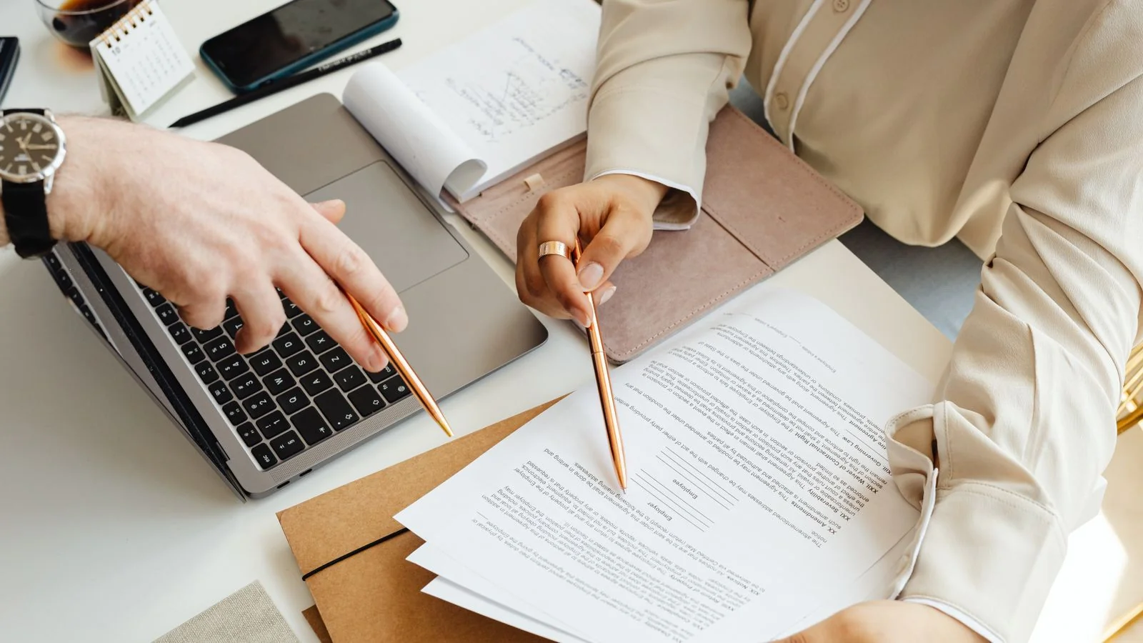 Two people reviewing documents together beside an open laptop.