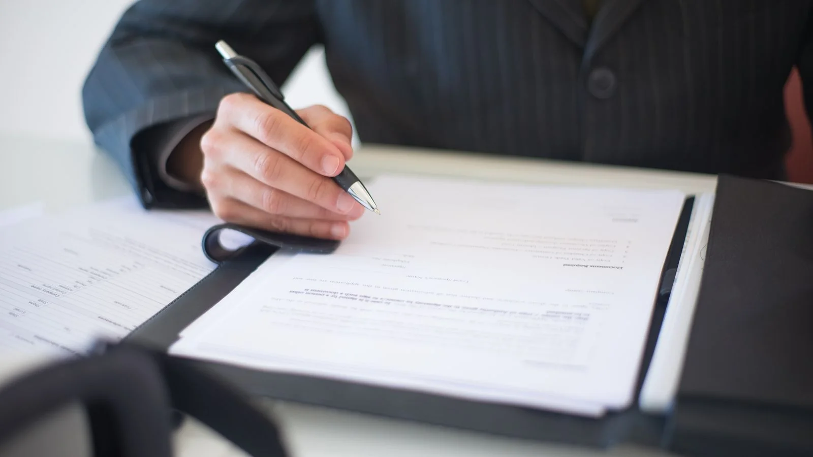 A hand signing a document with a pen on a desk.