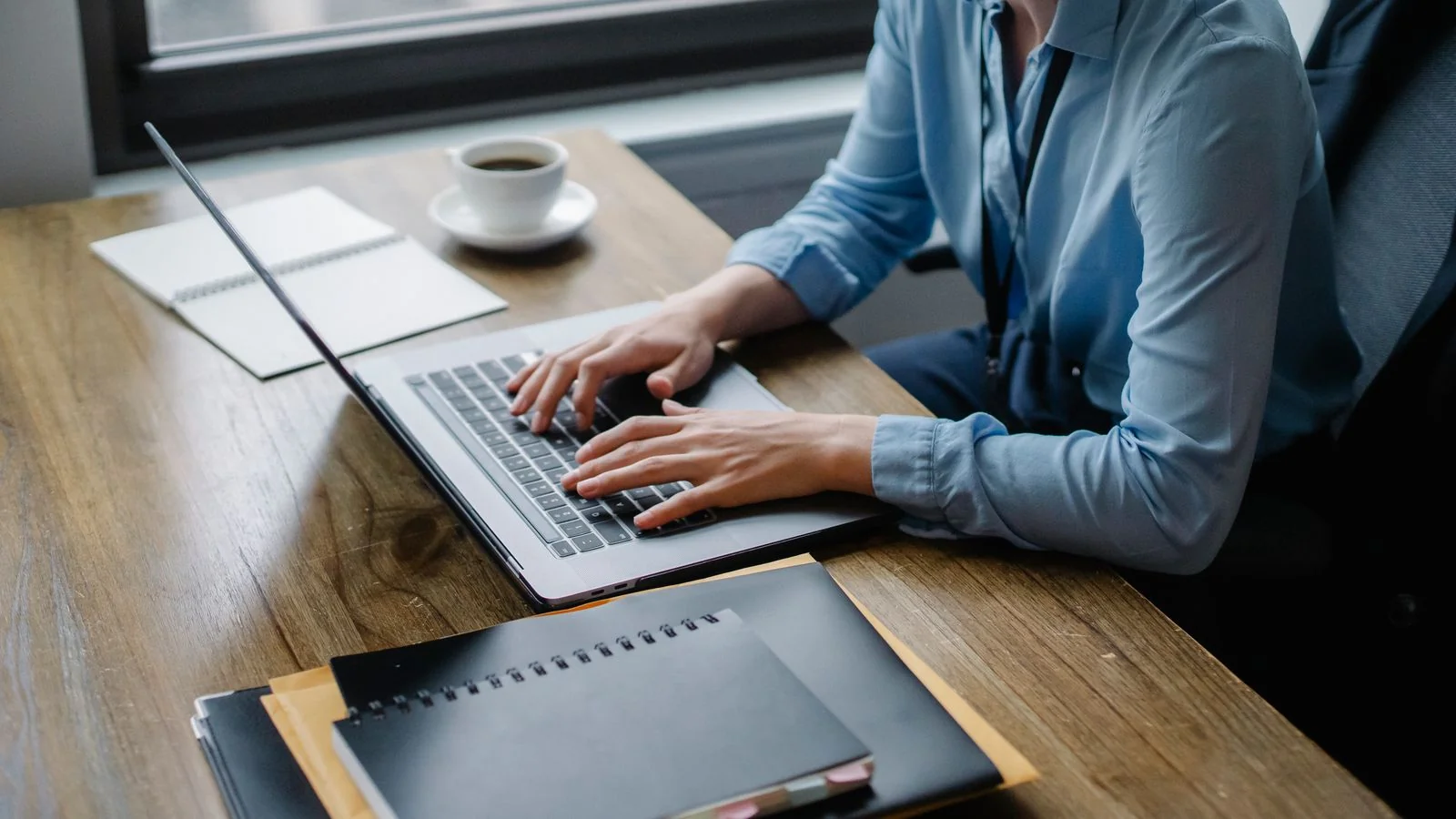 Office worker typing a draft on a laptop beside coffee and notebooks