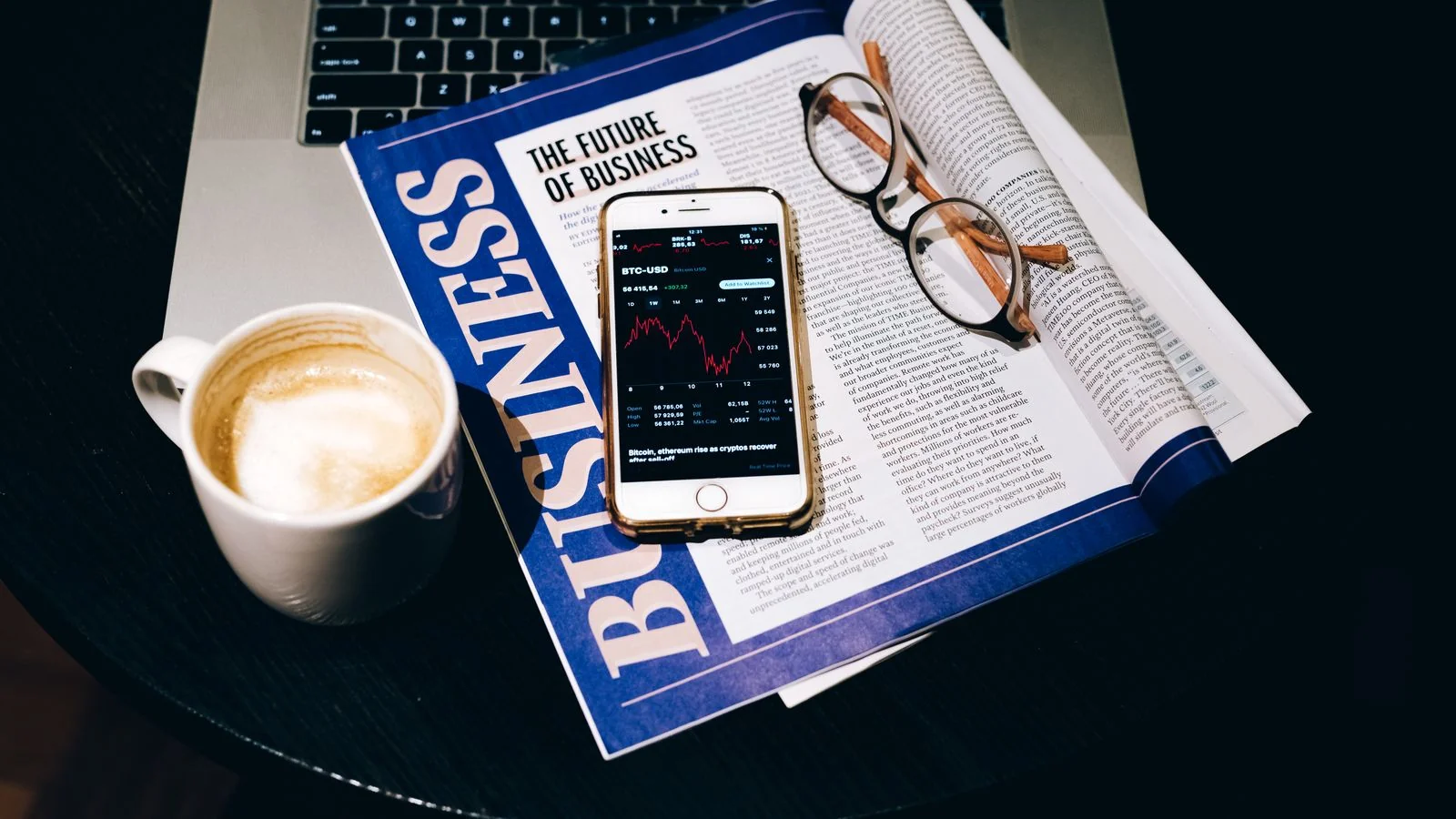 A desk with a laptop, coffee, and a newspaper, the finance news a release rides.