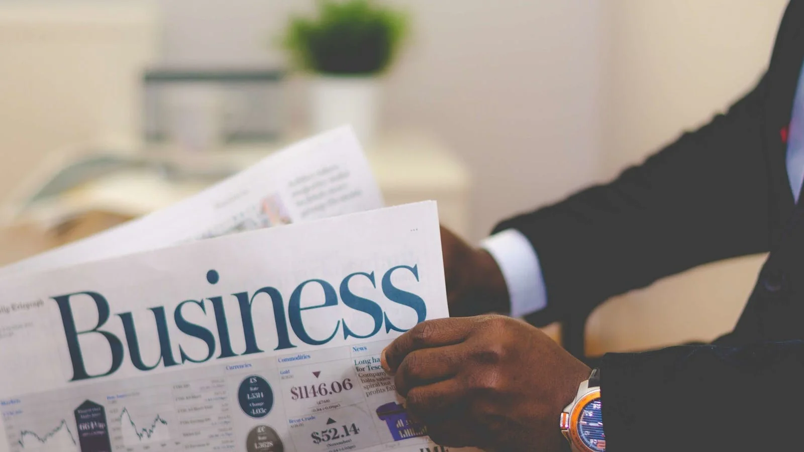Executive reading a folded business newspaper, scanning headlines for stories his firm might be in