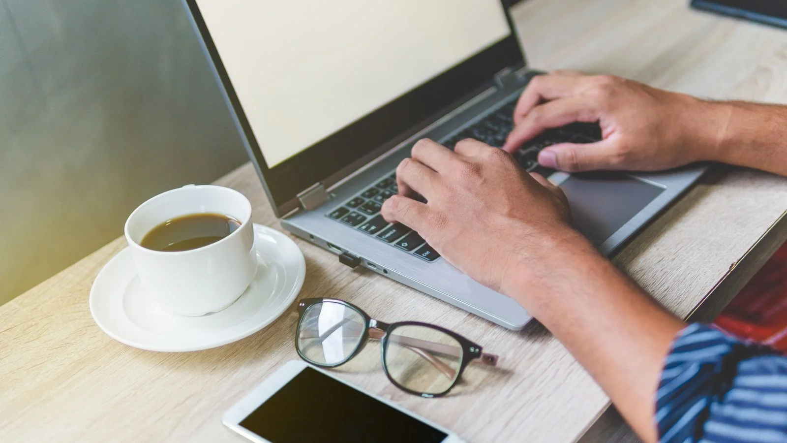 A laptop, coffee and notebook on a desk where the release actually gets written