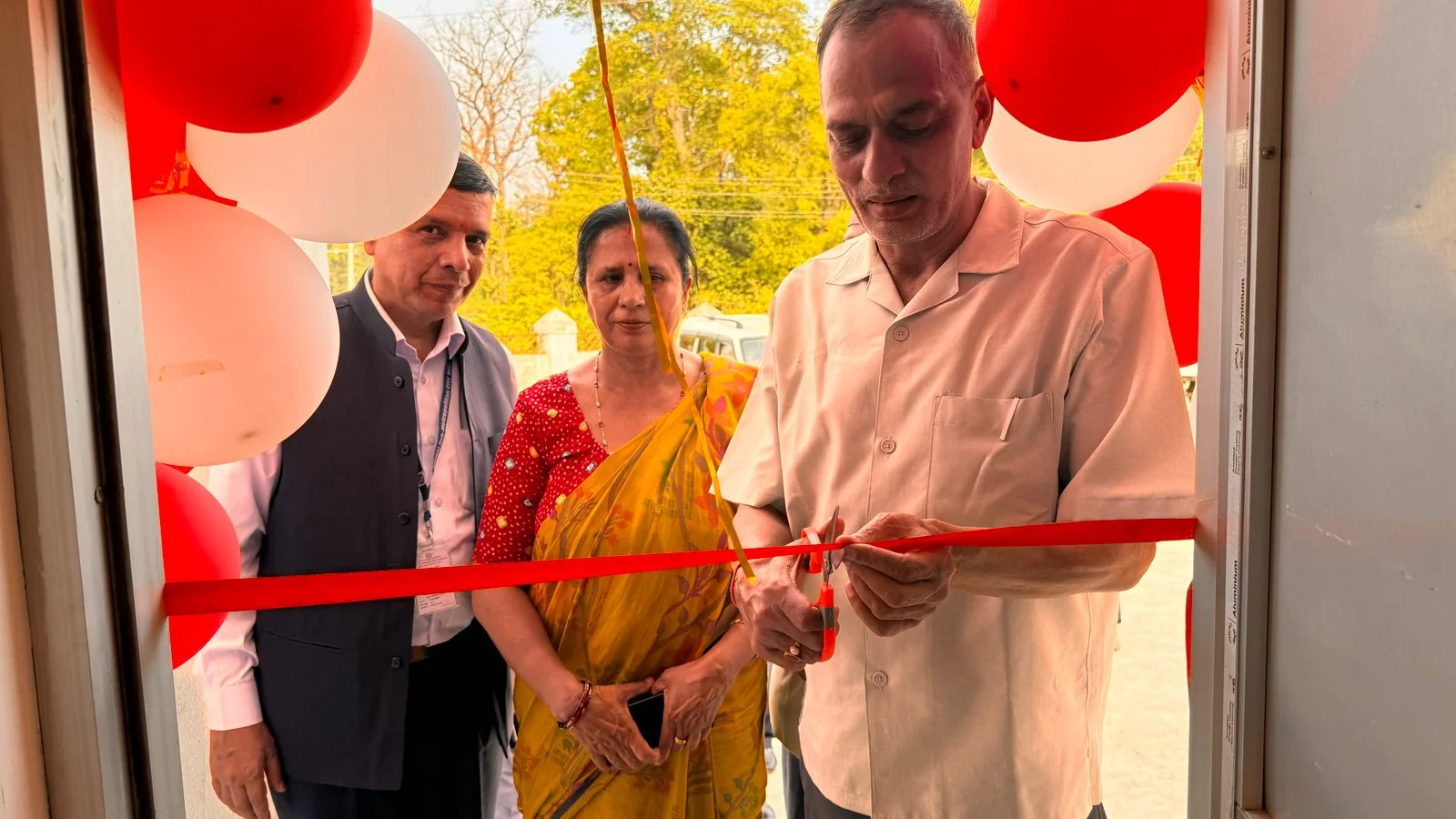 Clinic owners cut a red ribbon among red and white balloons at a new physical therapy clinic opening.