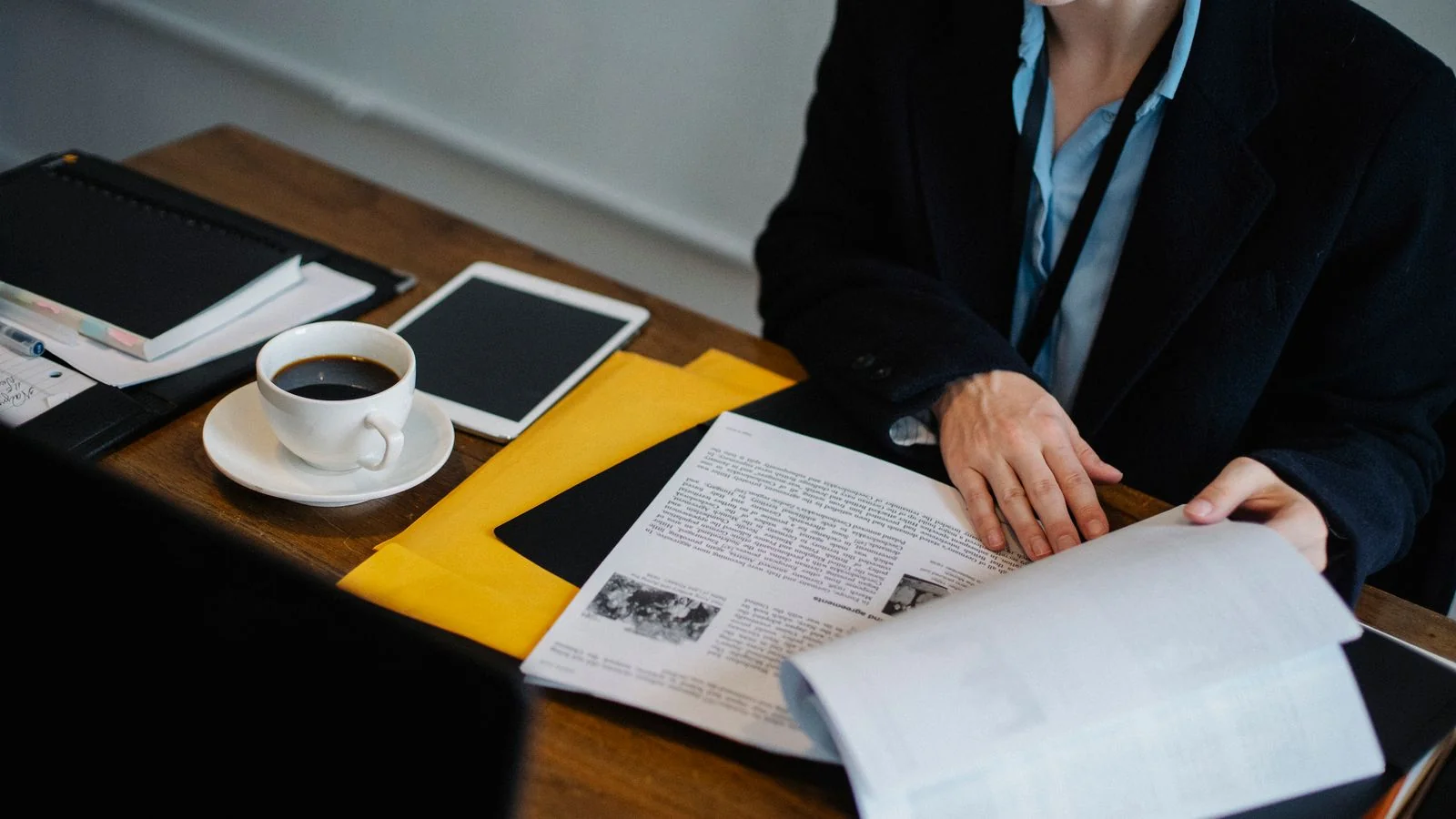 A businesswoman at a desk reviewing documents with a tablet and coffee.
