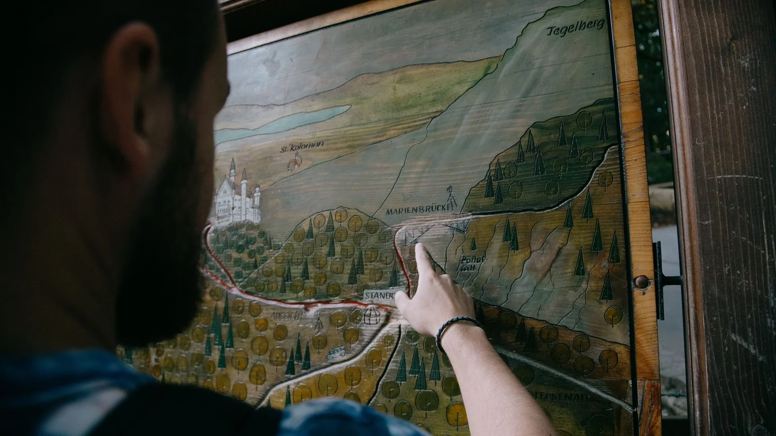 A guide pointing to a carved relief map of mountains and roads, the access question every travel story turns on.