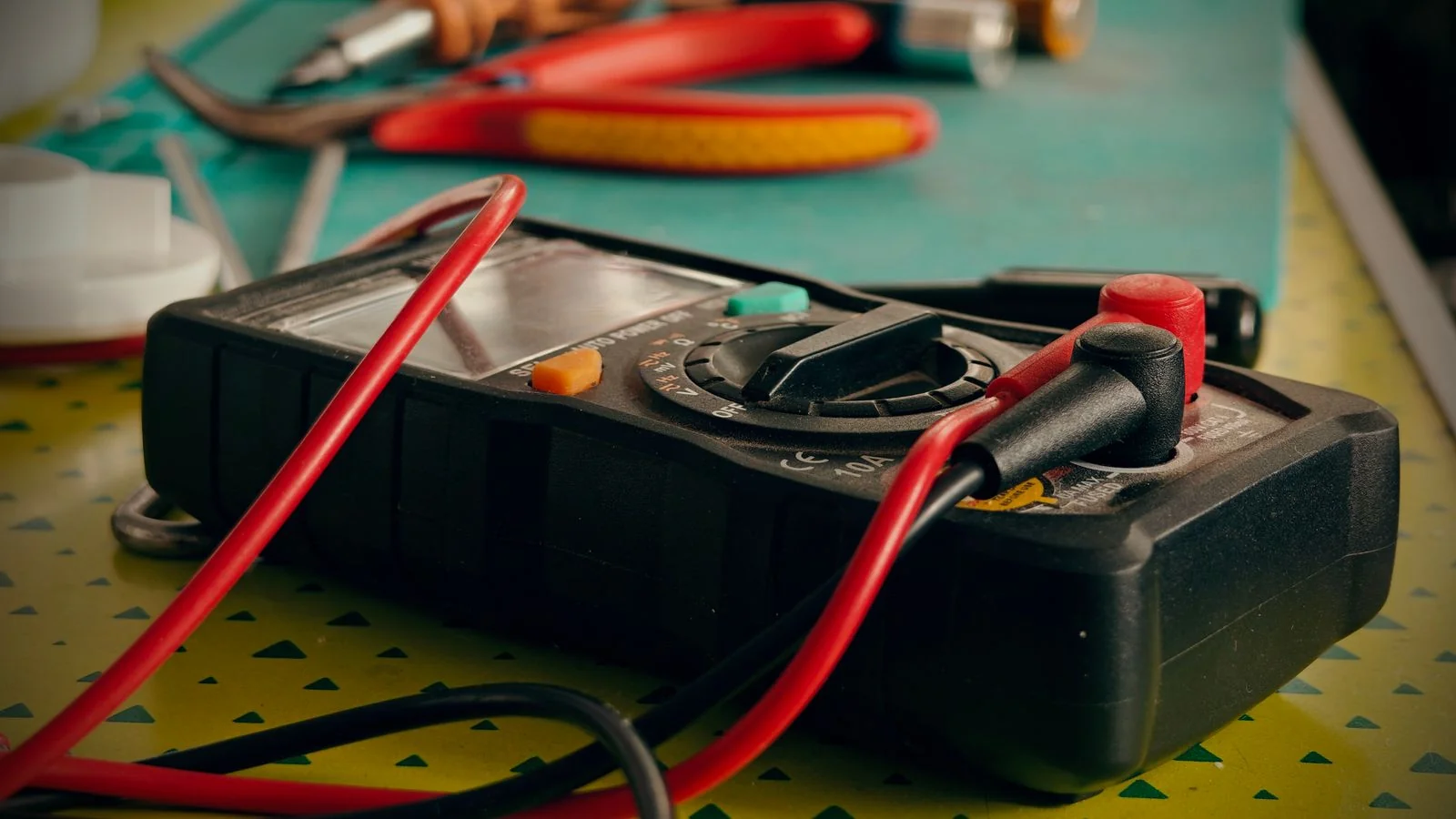 A multimeter and hand tools laid out on a workbench, the specifics that make a trade story concrete