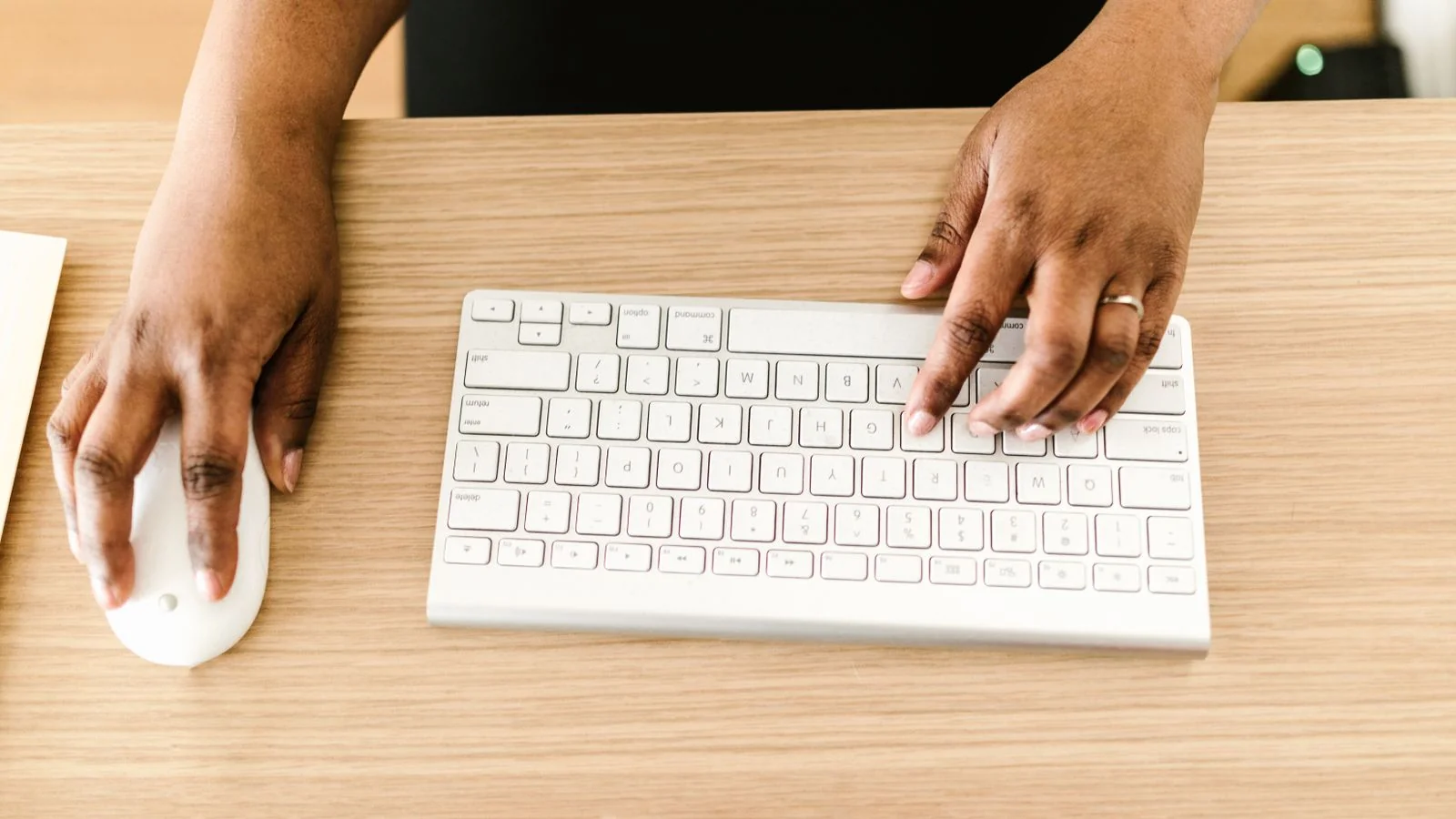 Hands typing on a white keyboard at a wooden desk.
