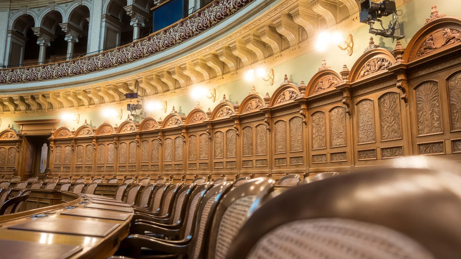 An empty legislative council chamber with curved seating and ornate detail.