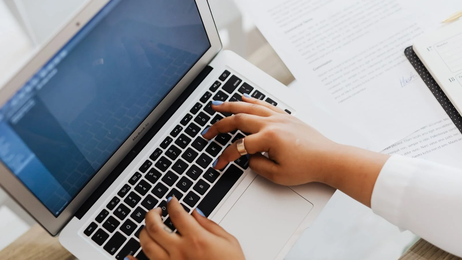 Hands typing on a laptop surrounded by papers, drafting a press release.