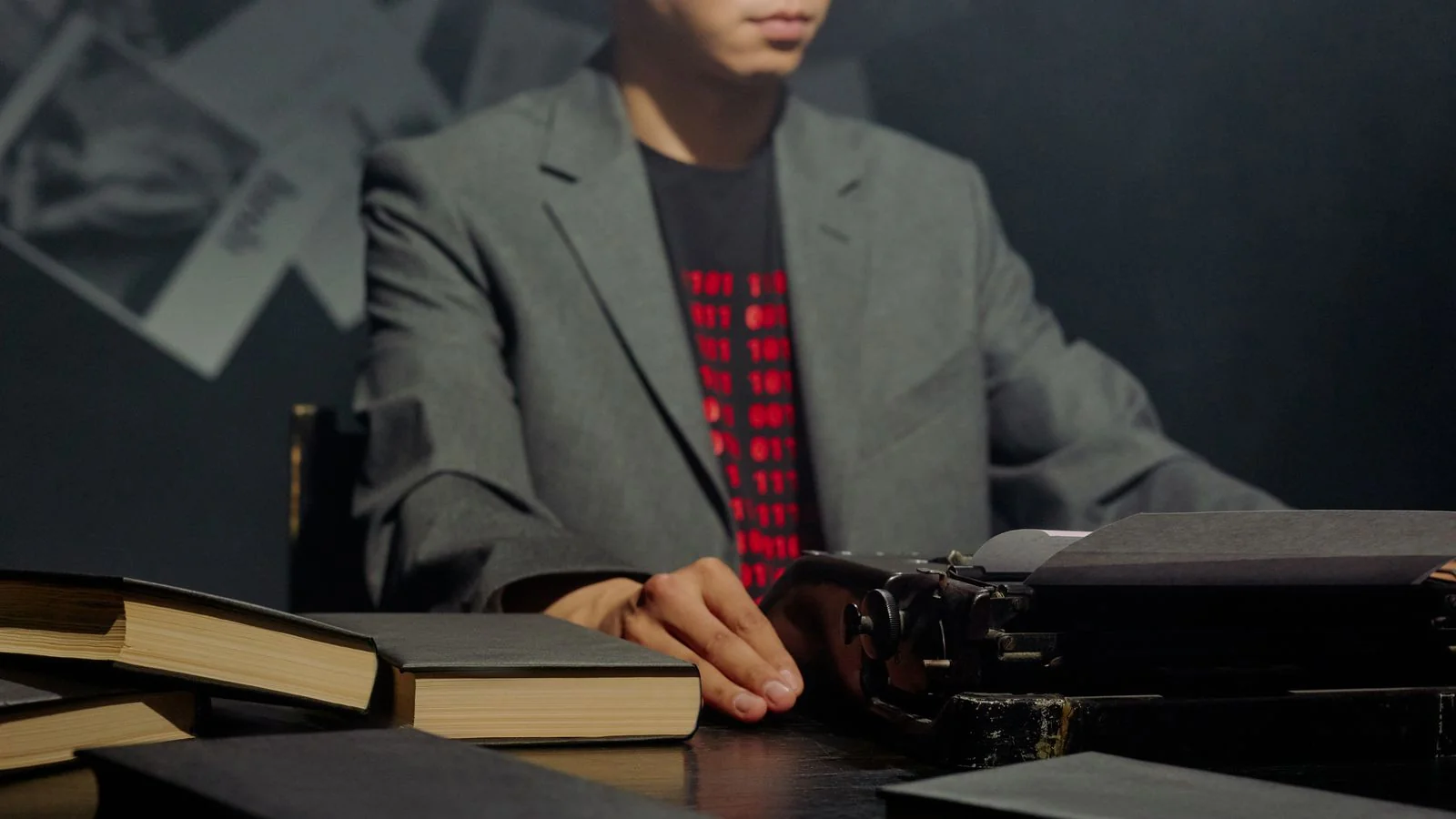 A man in a blazer typing on a classic typewriter surrounded by books