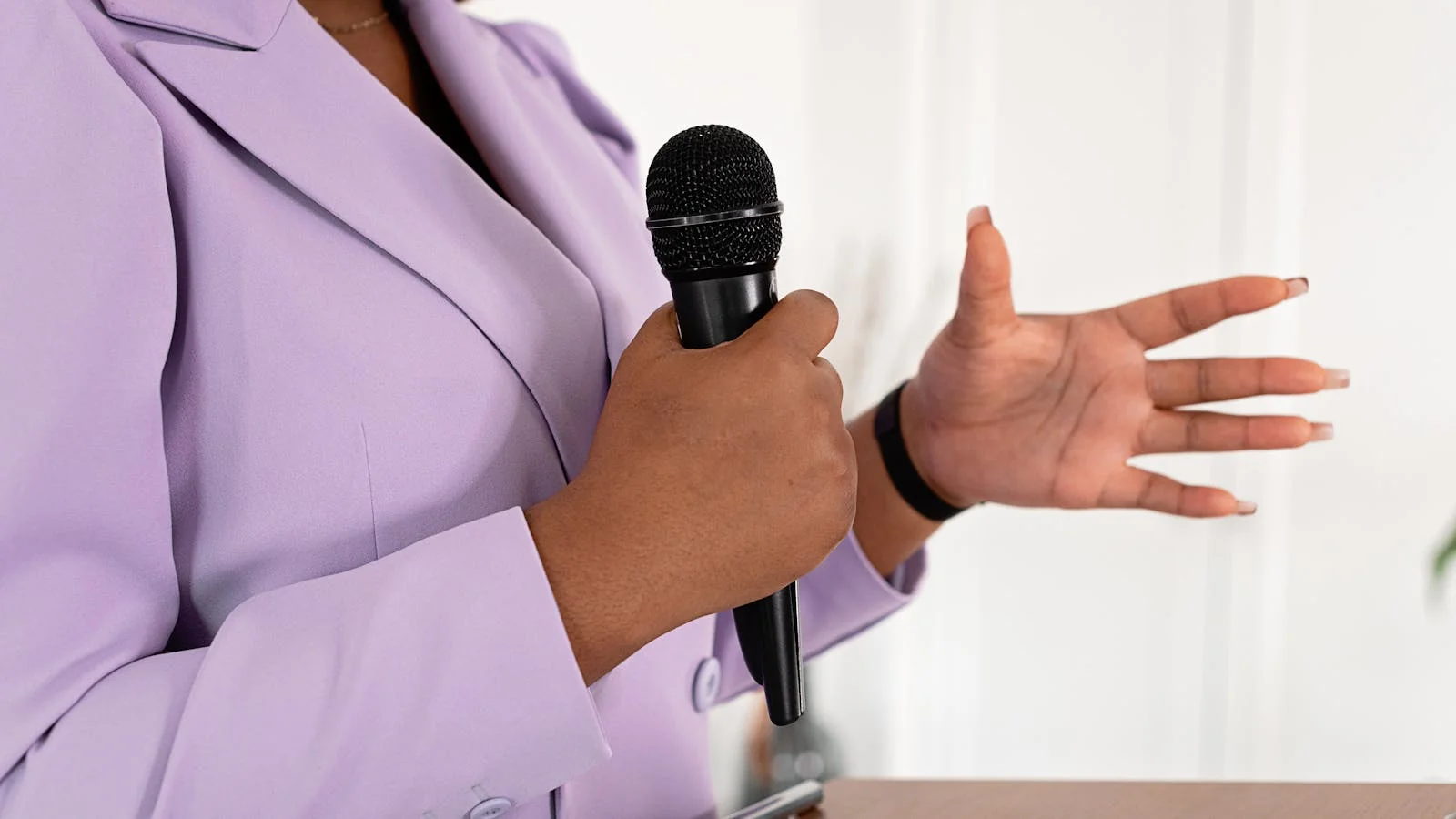 A professional delivering a pitch with a microphone, gesturing to make a point.