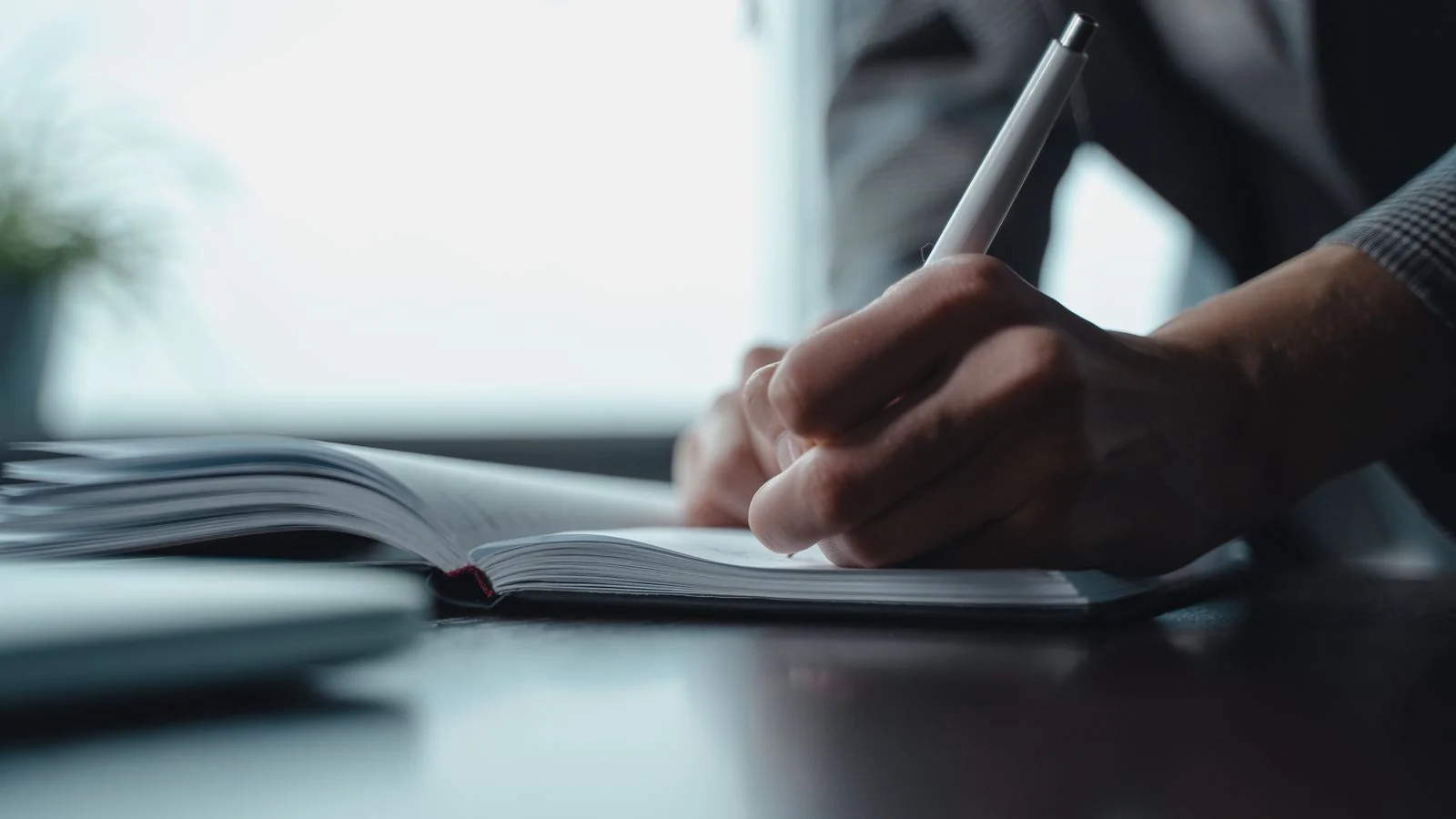 Close-up of a person writing in a notebook with a pen, the treatment Chief Executive asks for before any draft