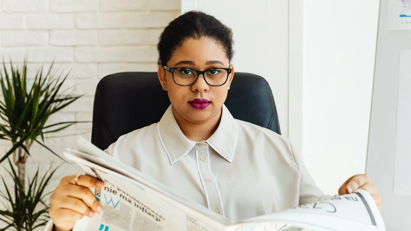 Woman in glasses reading a newspaper at her office desk, the kind of reader who scans Views each morning