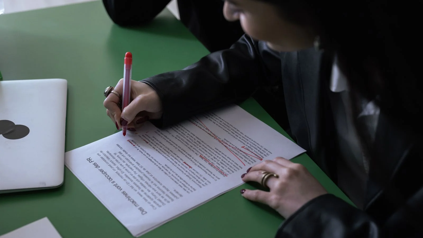 Woman in a suit editing a printed document with a red pen beside a laptop, the review work a board seat means