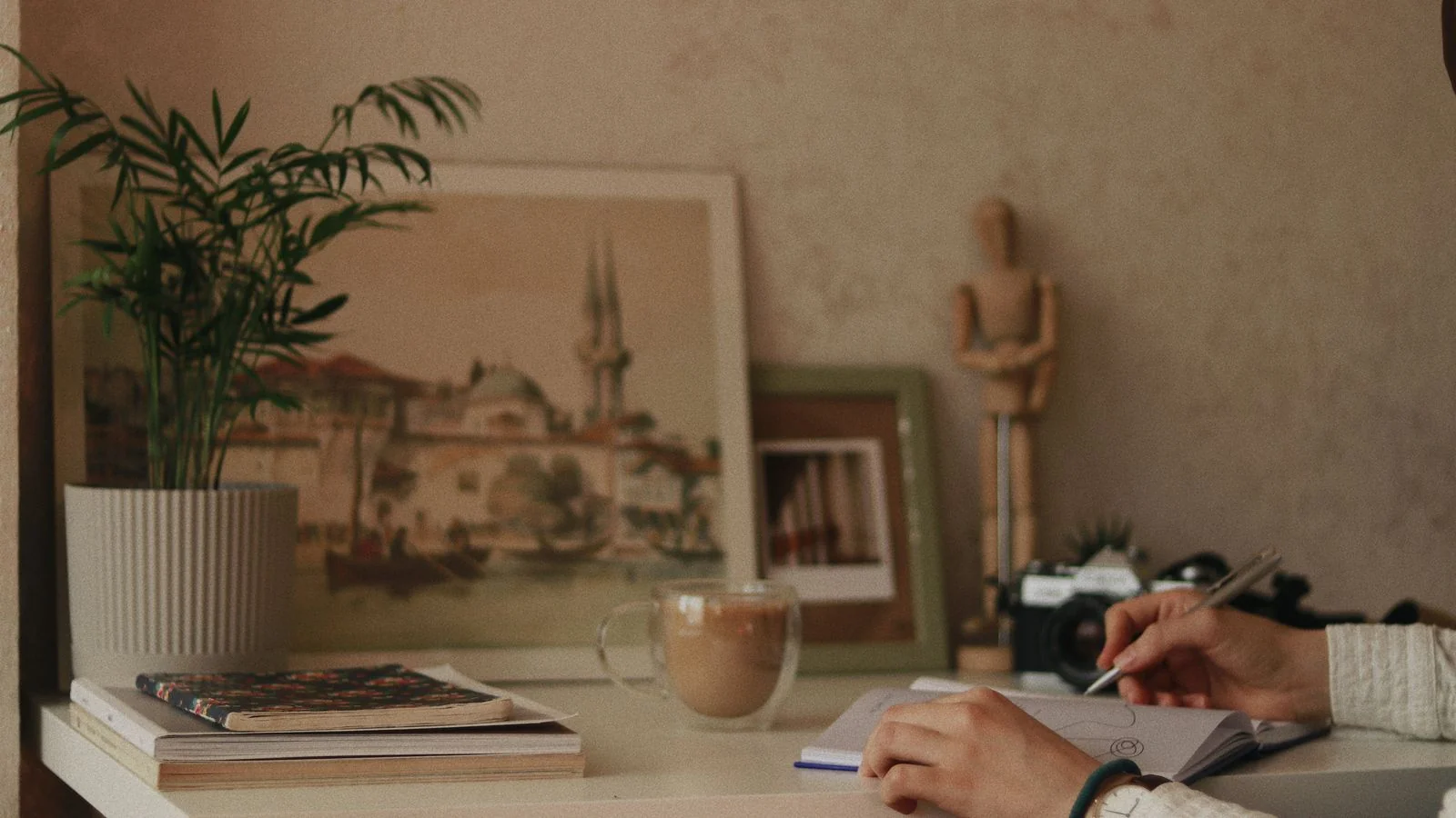 Someone writing in a notebook beside coffee and plants, the drafting work that follows a cleared pitch