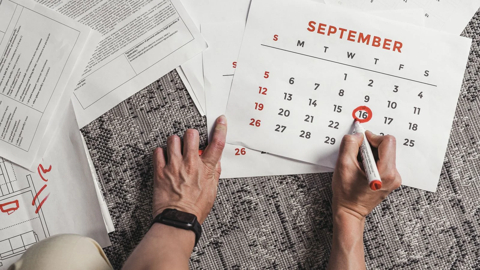 Hands holding a calendar with dates circled, surrounded by documents, the monthly cadence the role demands